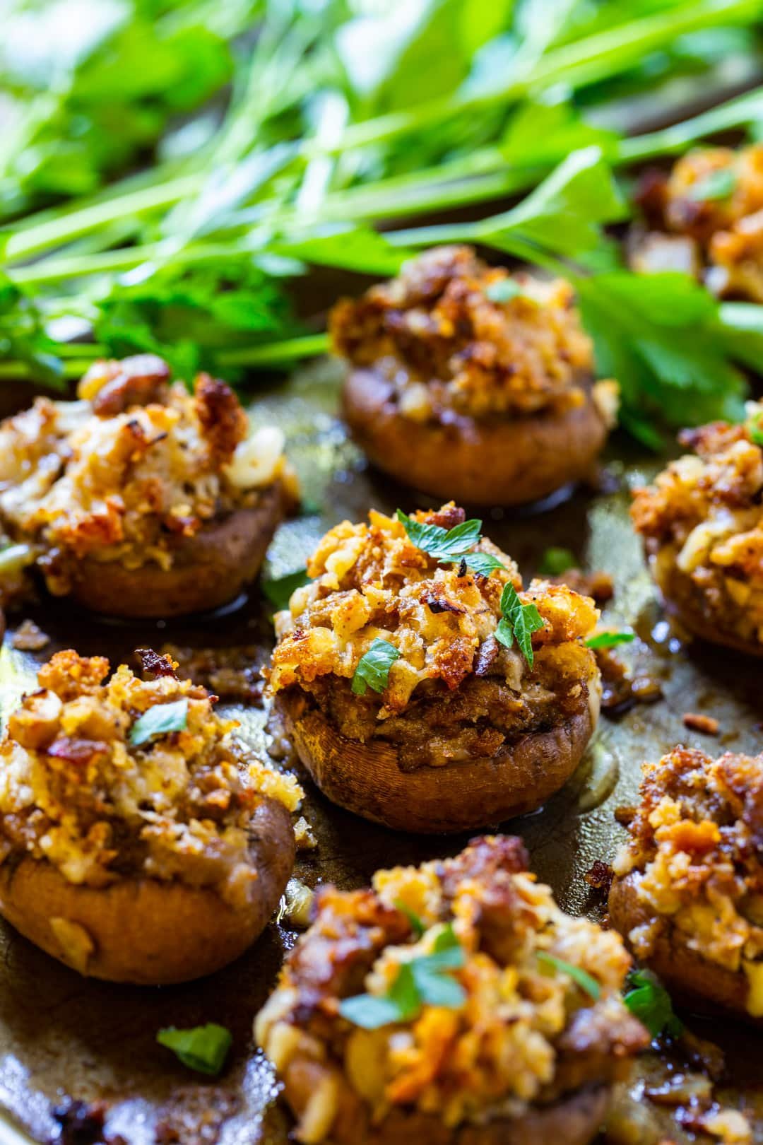 Mushrooms stuffed with sausage on baking sheet with fresh parsley.