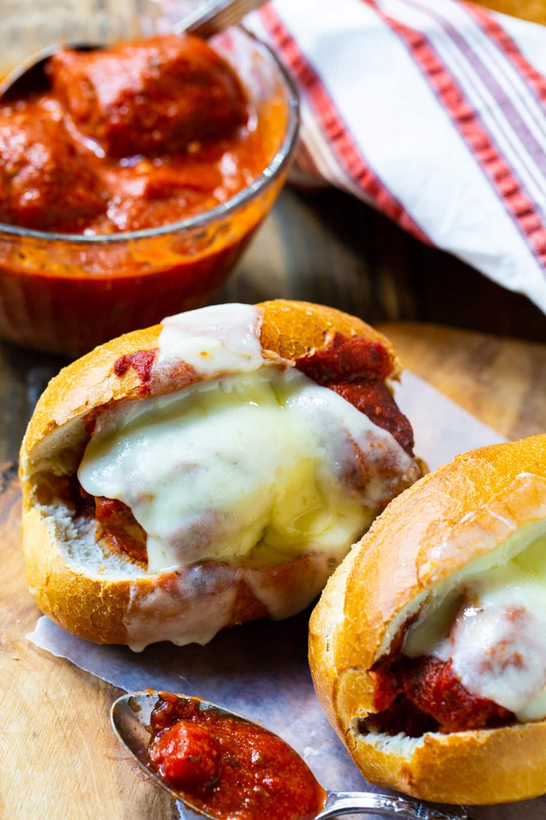 Two Meatball Subs on a wood cutting board.