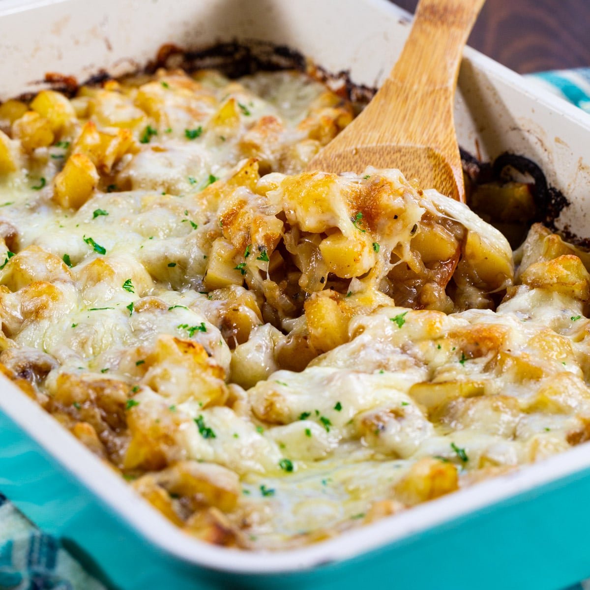 Spoon scooping French Onion Potatoes out of baking dish.