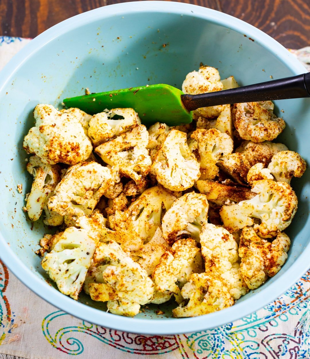 Uncooked cauliflower tossed with spices in a bowl.