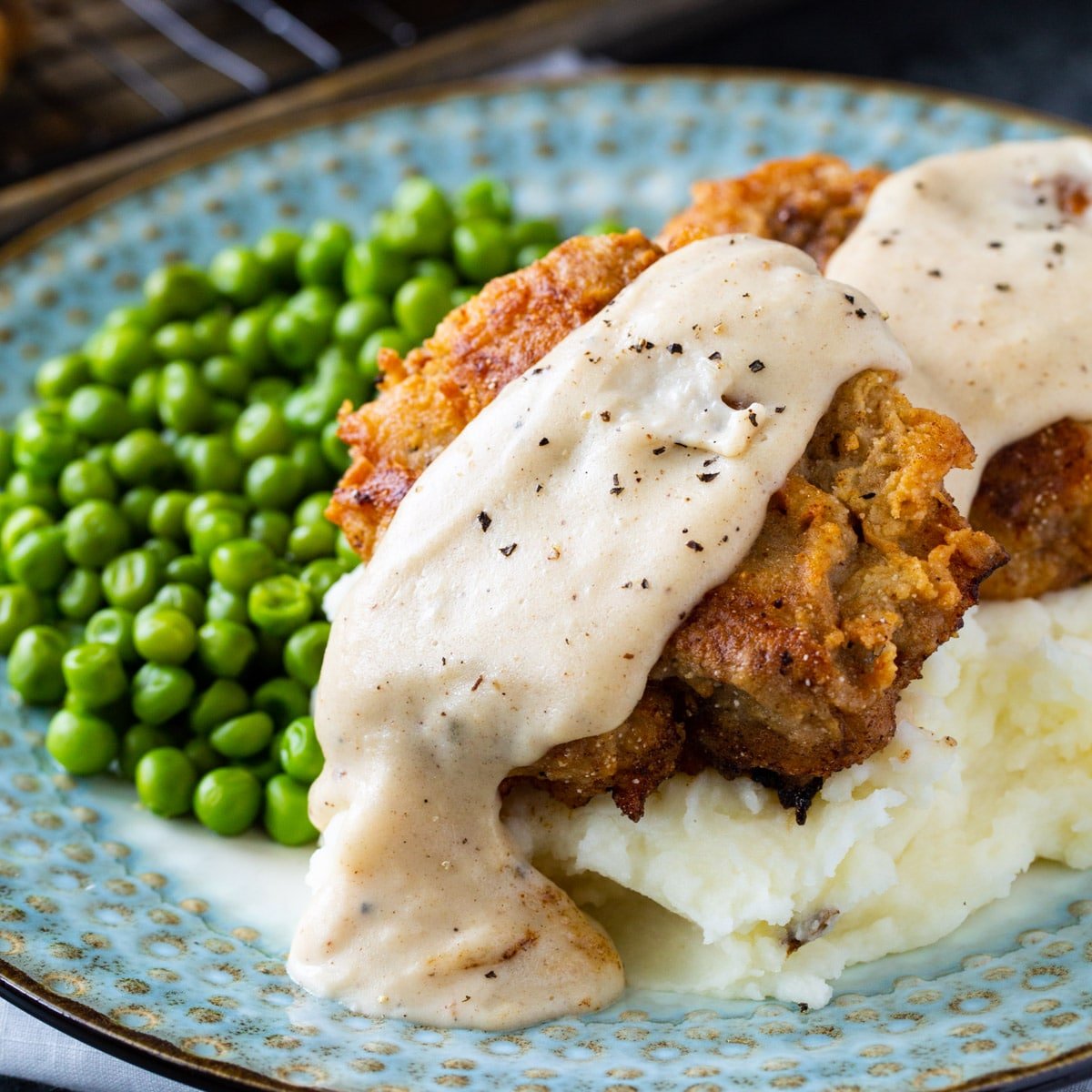 Chicken Fried Steak with White Gravy over mashed potatoes with a side of peas.