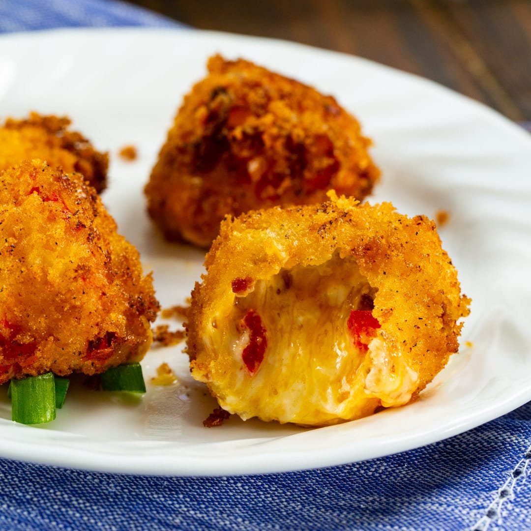 Three Fried Pimento Cheese Balls on a plate with one bitten into.