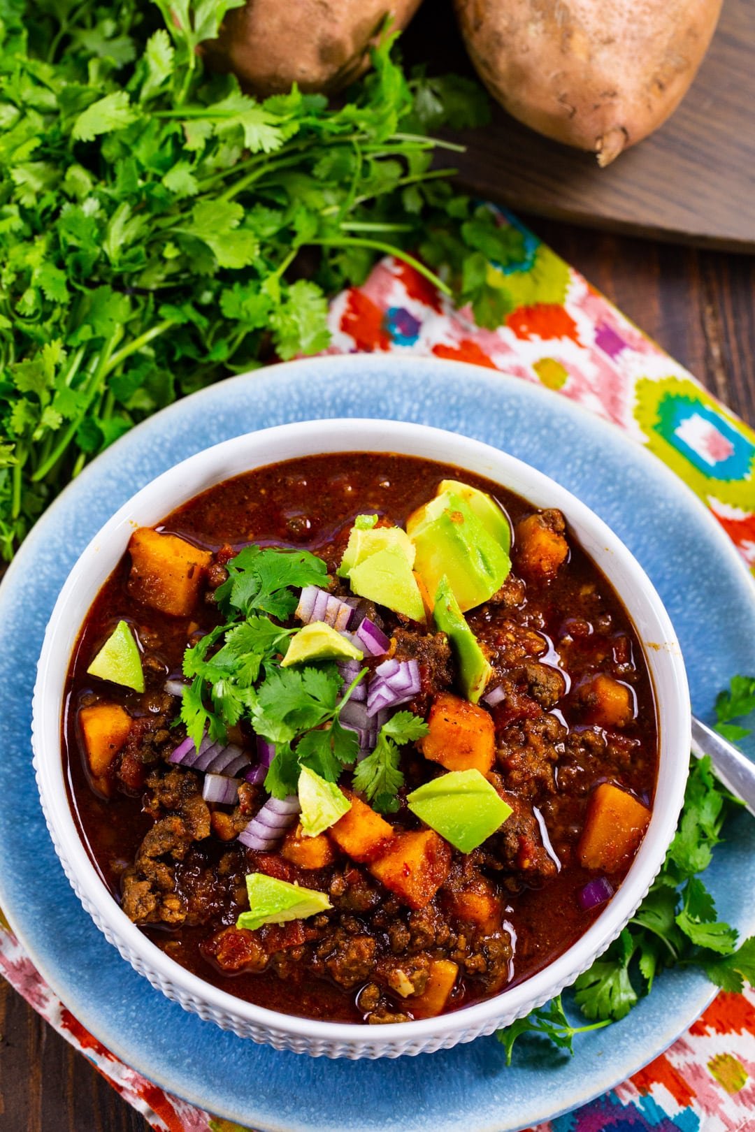 Beef and Sweet Potato Chili topped with avocado and cilantro in a bowl.