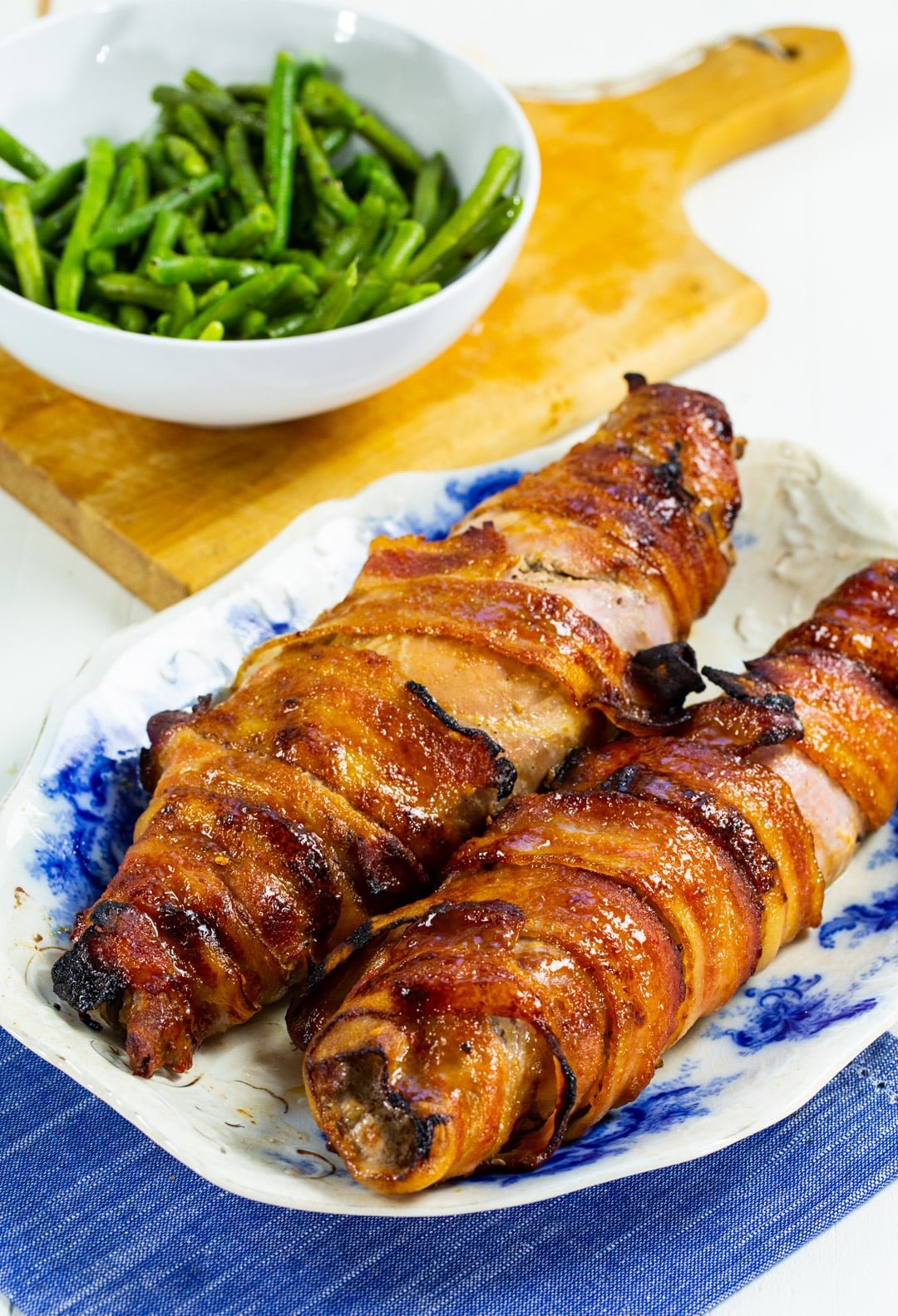 Brown Sugar Bacon Wrapped Pork Tenderloins on serving plate and bowl of green beans.