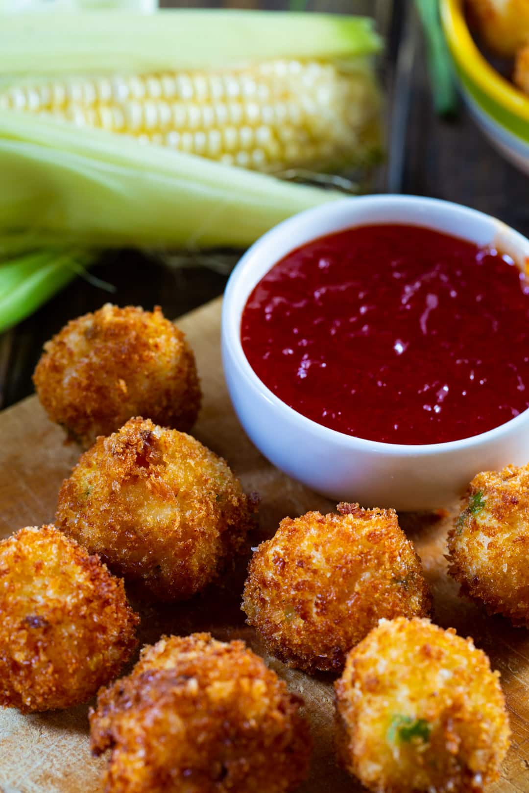 Crispy Fried Grits Fritters on wooden board with bowl of pepper jelly sauce.