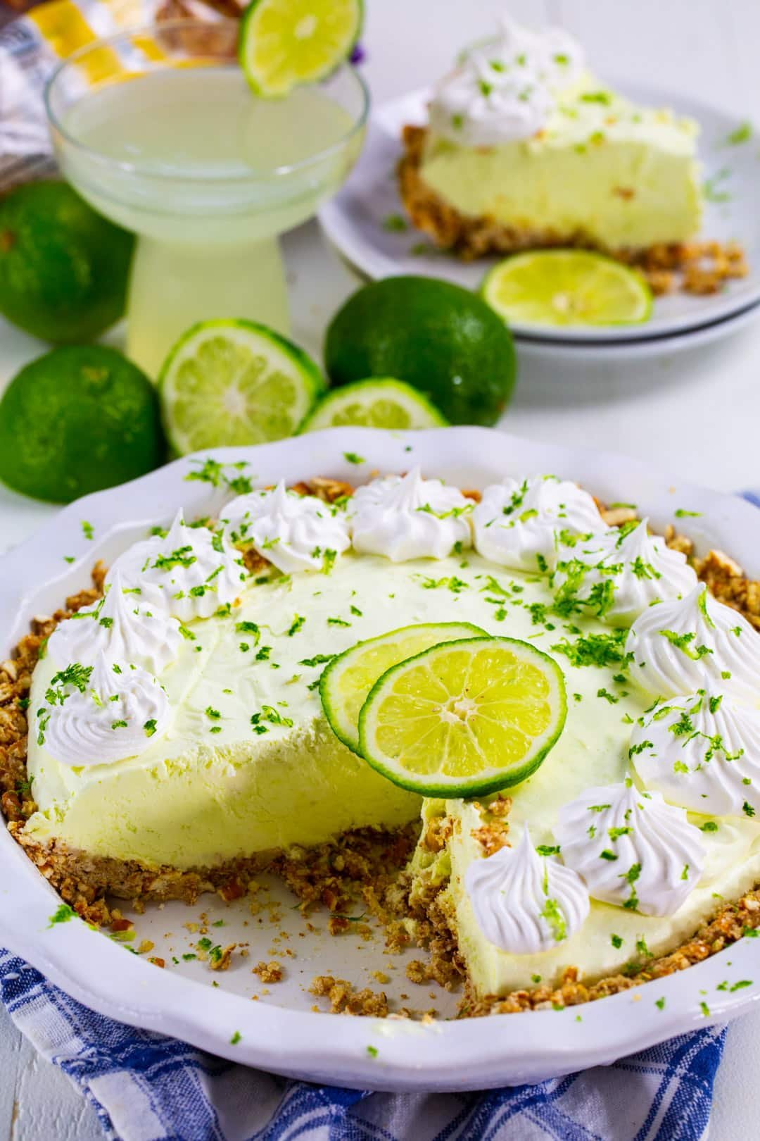 Pie in pie pan with fresh limes and margarita in background.