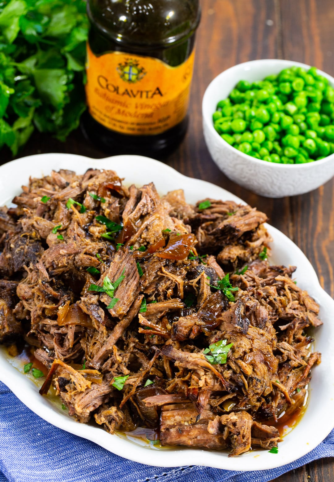 Crock Pot Balsamic Roast Beef on serving plate, bottle of vinegar, and bowl of peas