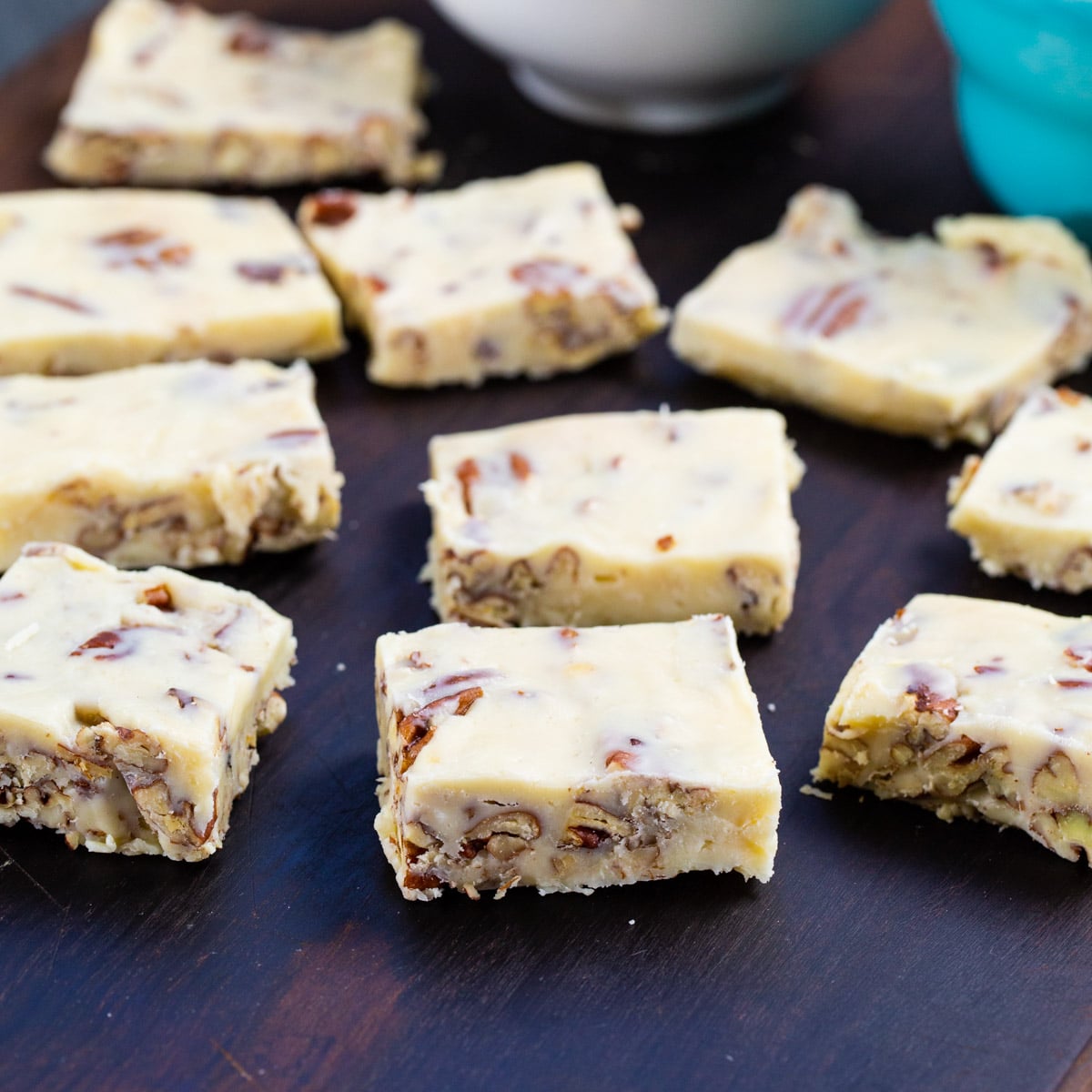 Squares of White Chocolate Pecan Candy on wooden board.