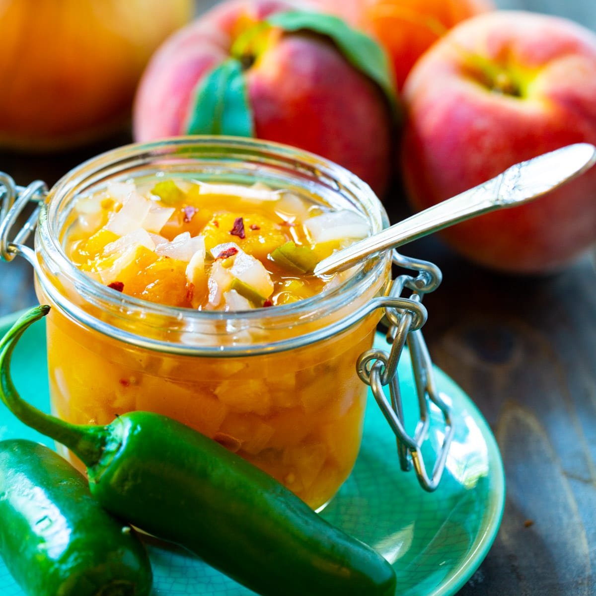 Peach-Vidalia Onion Relish successful  a solid  jar surrounded by fesh peaches.