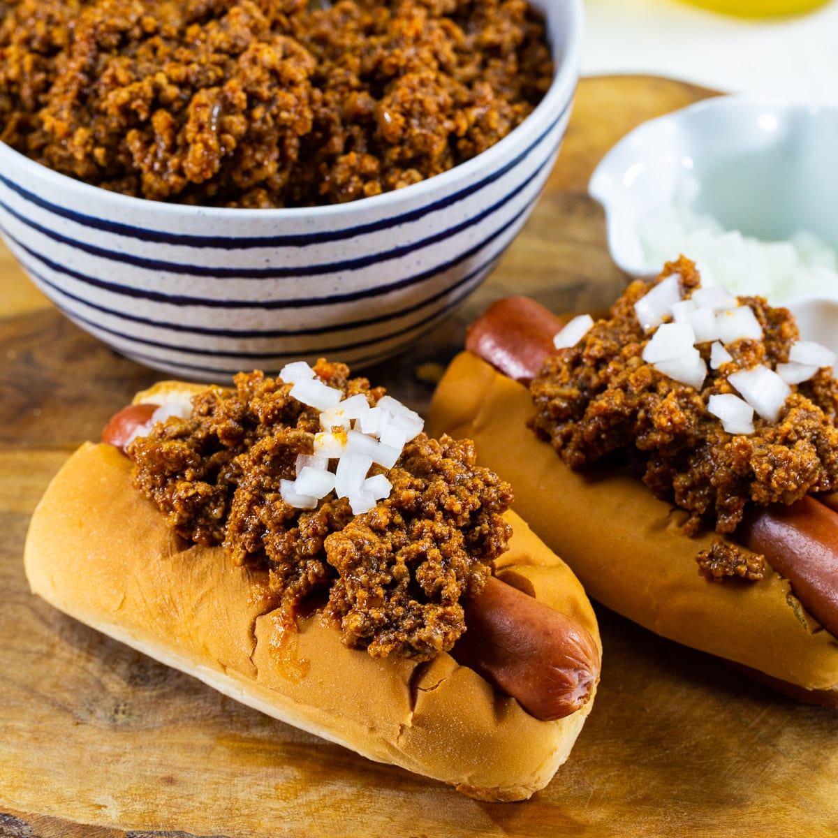 Two hot dogs topped with chili and onion.