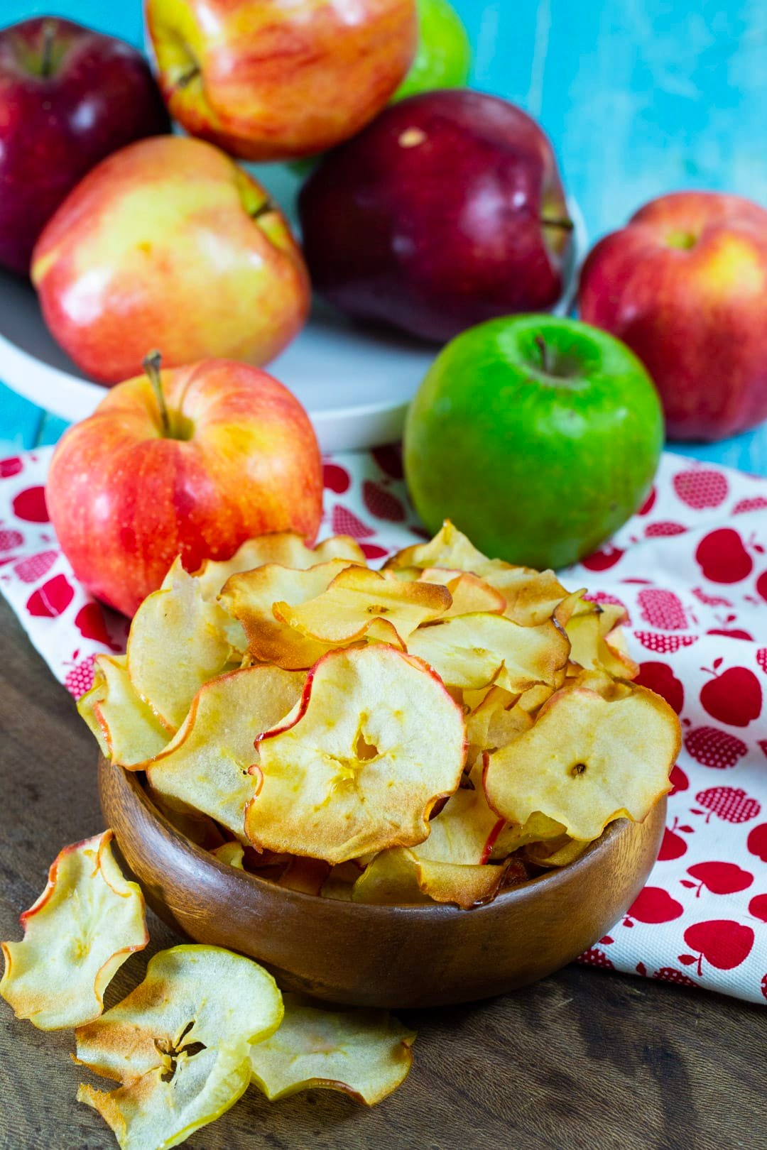 Apple chips in a bowl surrounded by fresh apples.