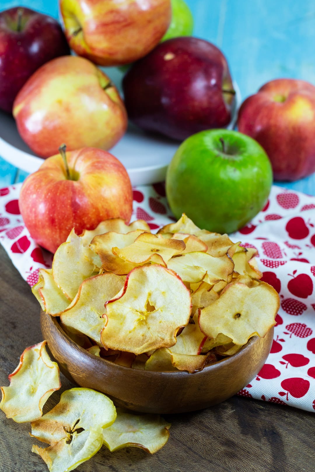 Apple chips in a bowl surrounded by fresh apples.