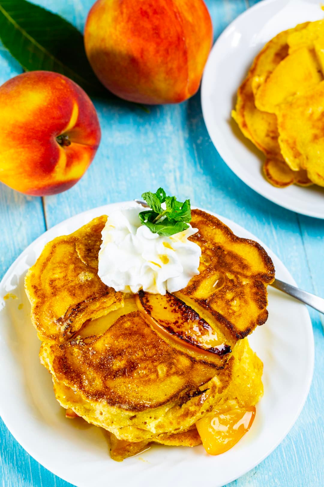 Pancakes stacked on a plate surrounded by fresh peaches.