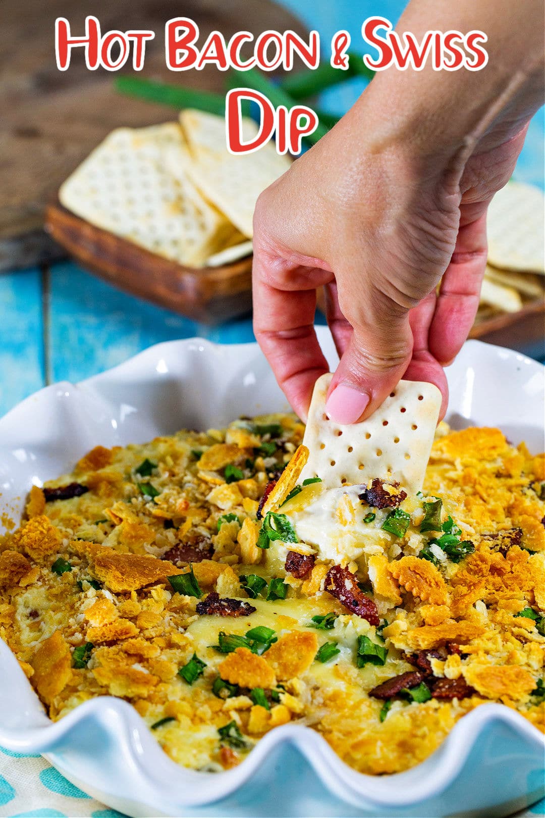 Hand dipping a cracker into Hot Bacon and Swiss Dip.