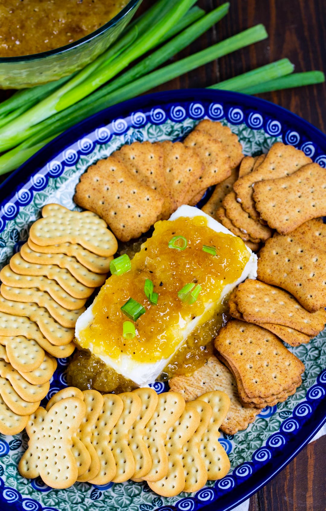 Cream cheese topped with sauce on a platter with crackers.