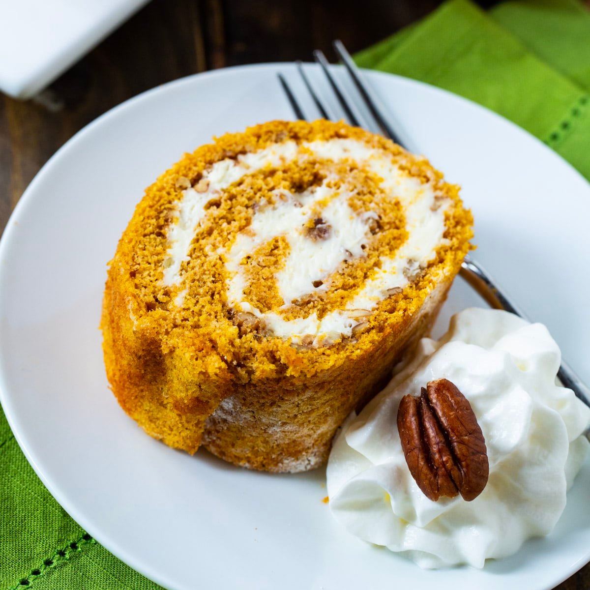 Piece of Pumpkin Cake Roll on plate with whipped cream.