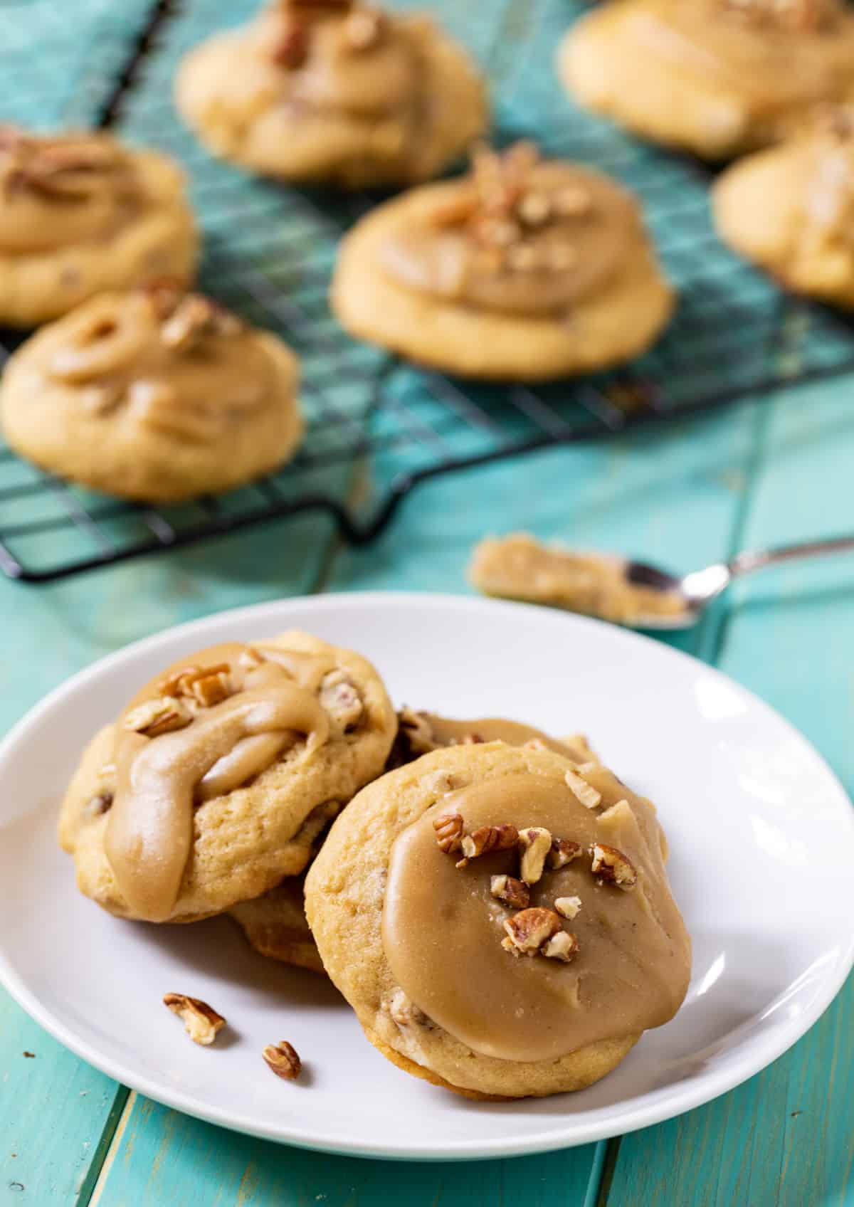 Caramel Frosted Brown Suagr Cookies on a plate and a wire rack.