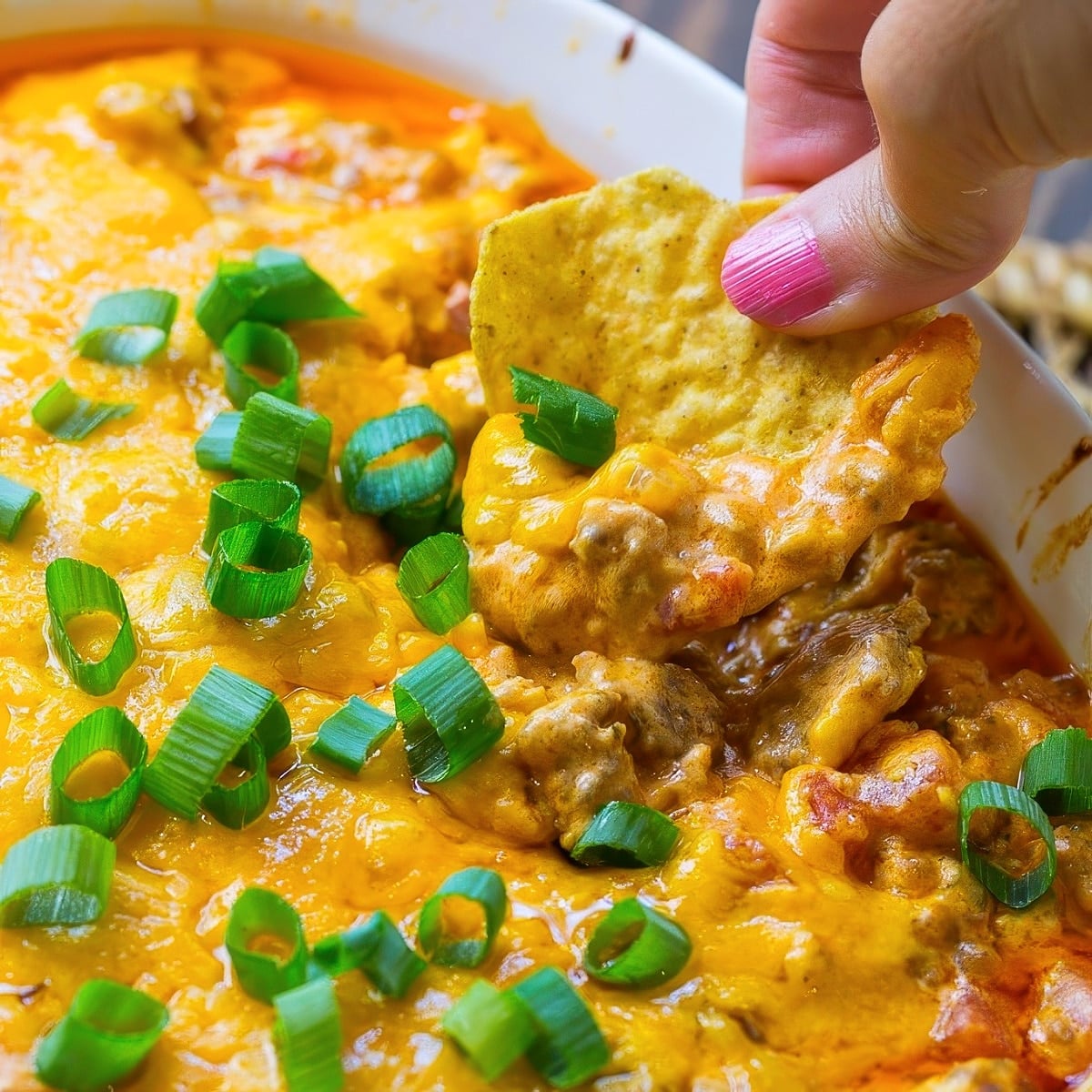 Chip scooping up Spicy Sausage Cheese Dip.