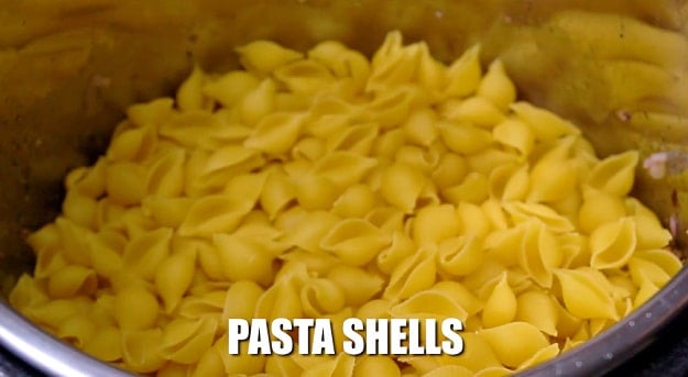 Adding uncooked pasta shells.