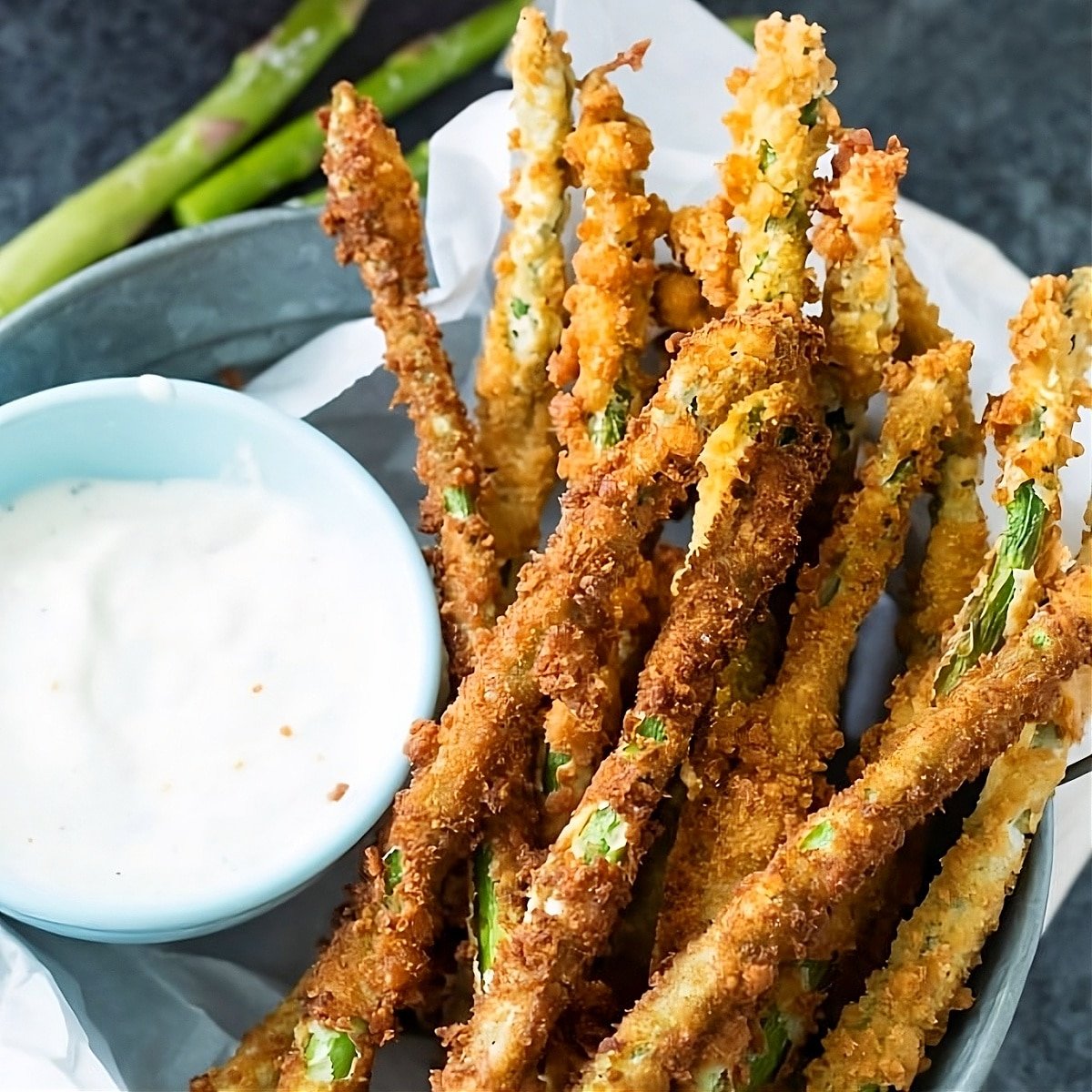 Fried Asparagus in a basket with ranch dressing in a bowl.