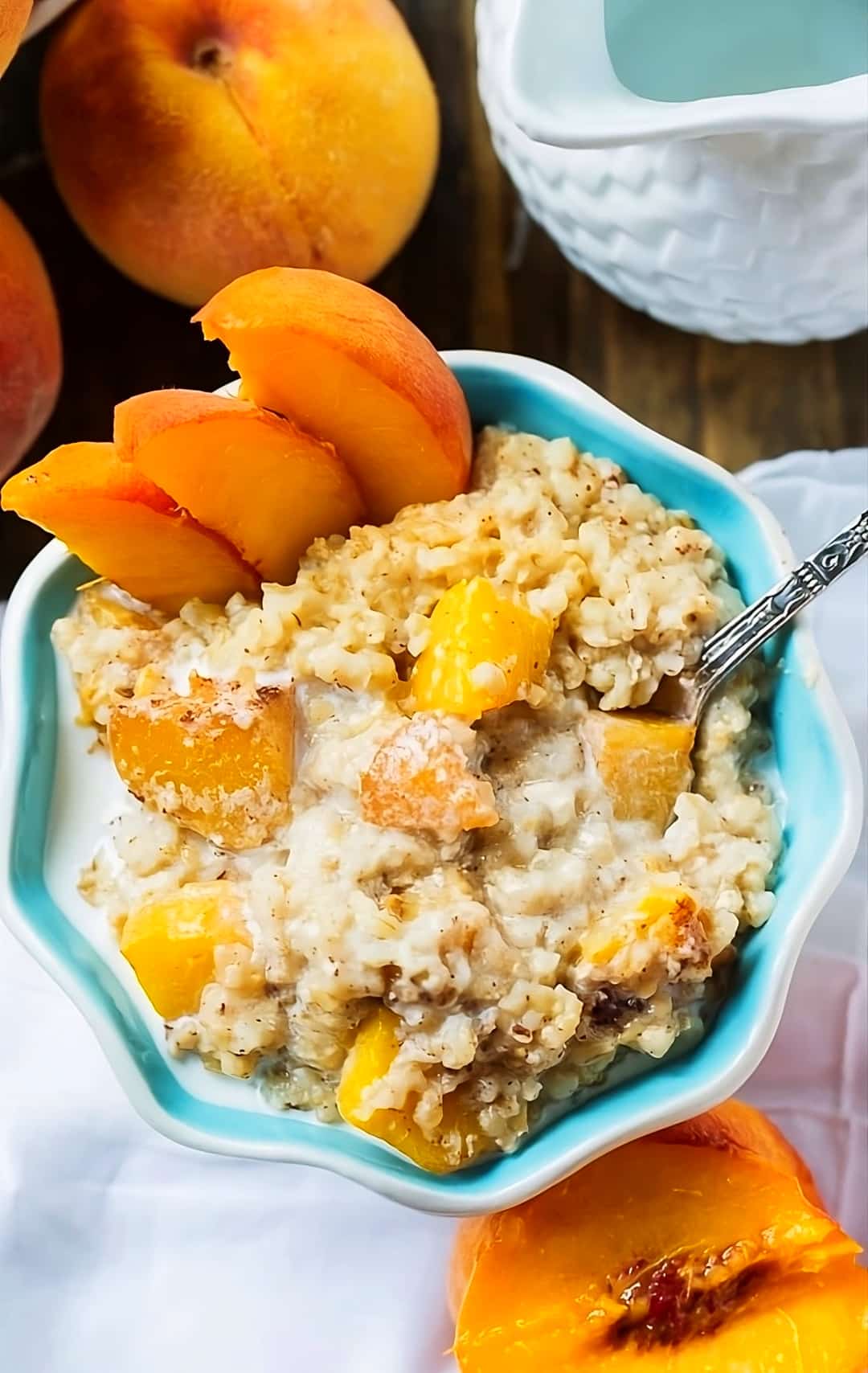 Crock Pot Peaches and Cream Oatmeal in a bowl surrounded by fresh peaches.