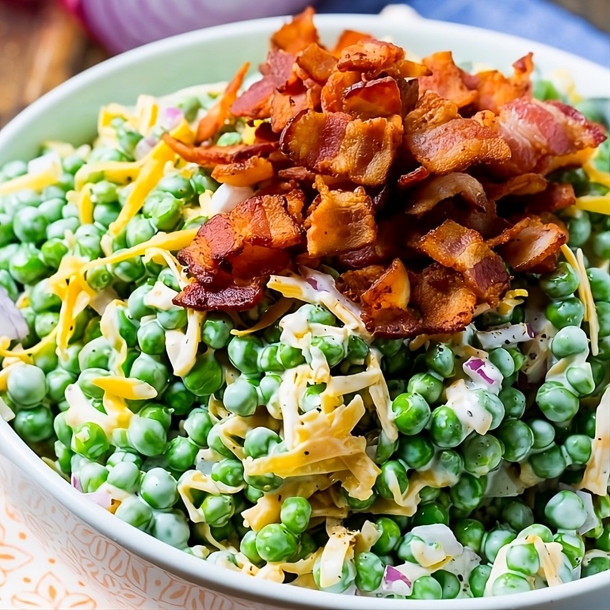 Creamy Pea Salad topped with bacon in a serving bowl.