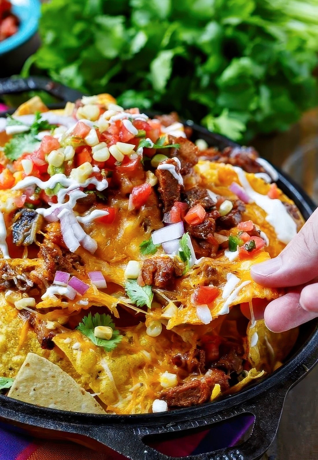 Hand pulling out a chip from pile of BBQ Brisket Nachos.