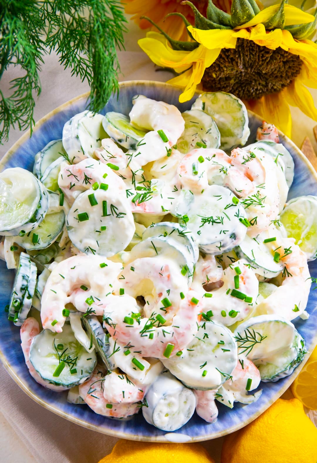 Shrimp Cucumber Salad in a blue serving bowl surrounded by lemons and flowers.