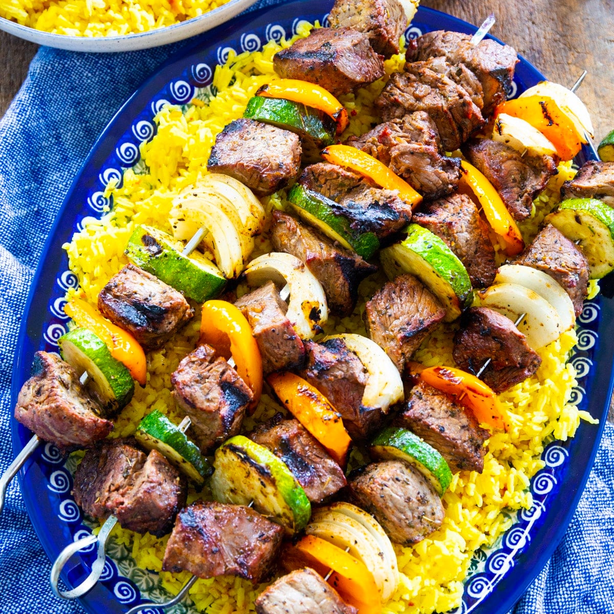 Grilled Beef Shish Kabobs over yellow rice on a serving platter.