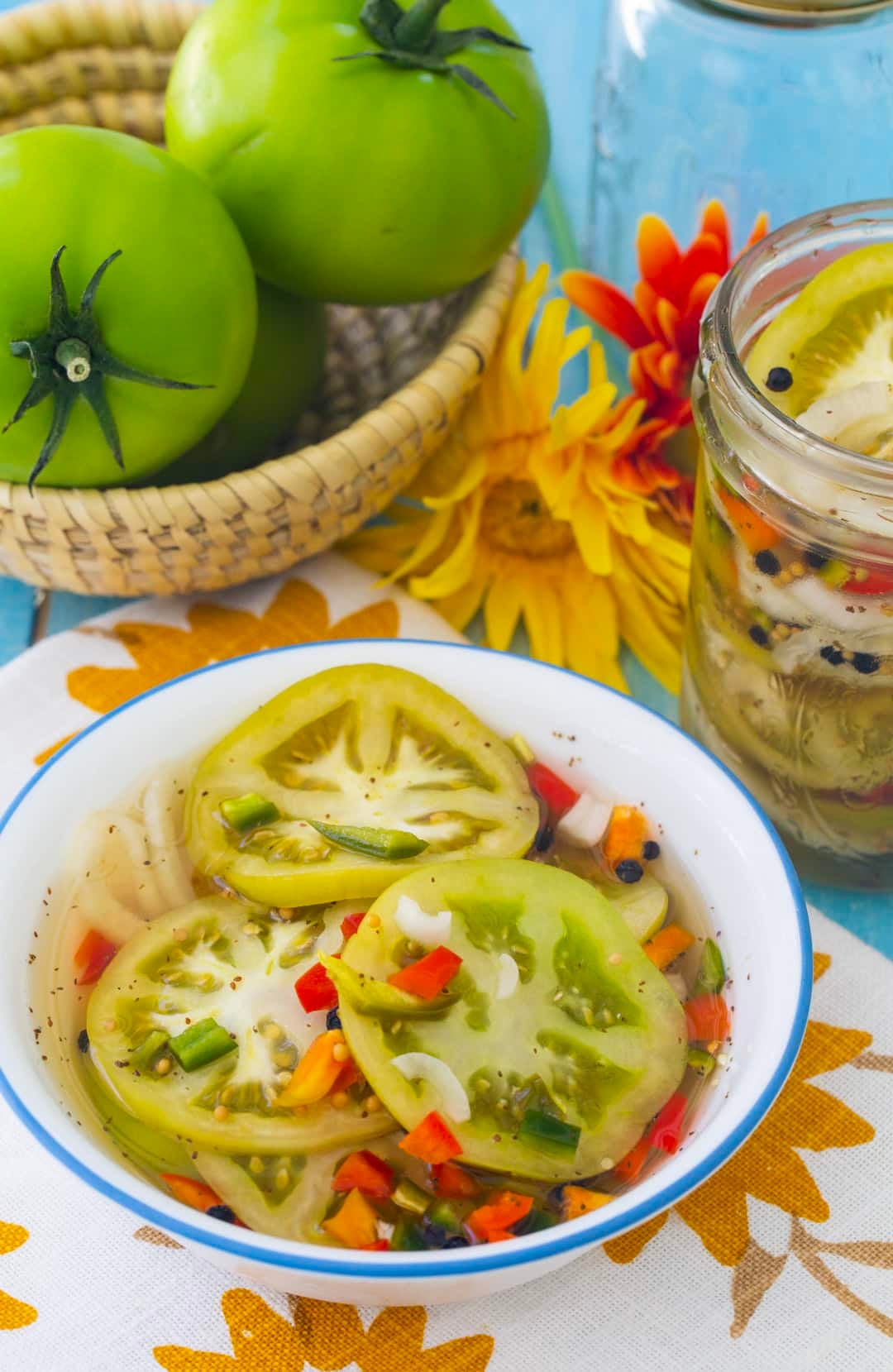 Pickled Green Tomatoes in a bowl with whole green tomatoes in background.