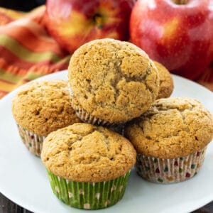 Muffins on a white plate with apples in background.