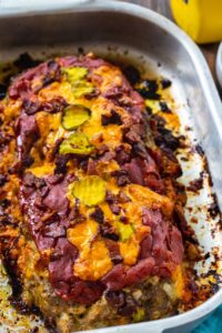 Meatloaf topped with bacon and cheddar cheese in baking pan.