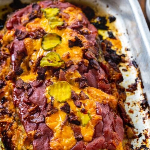 Meatloaf topped with bacon and cheddar cheese in baking pan.