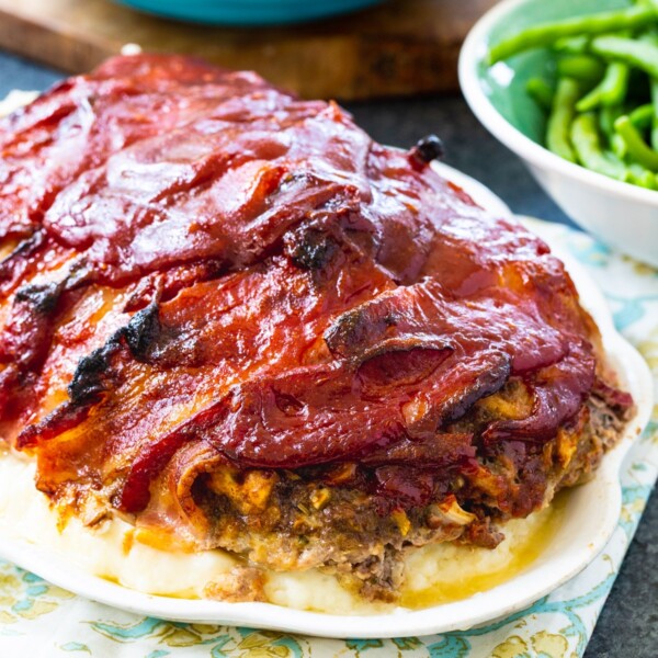 Bacon Wrapped Meatloaf over mashed poatoes on a serving platter.