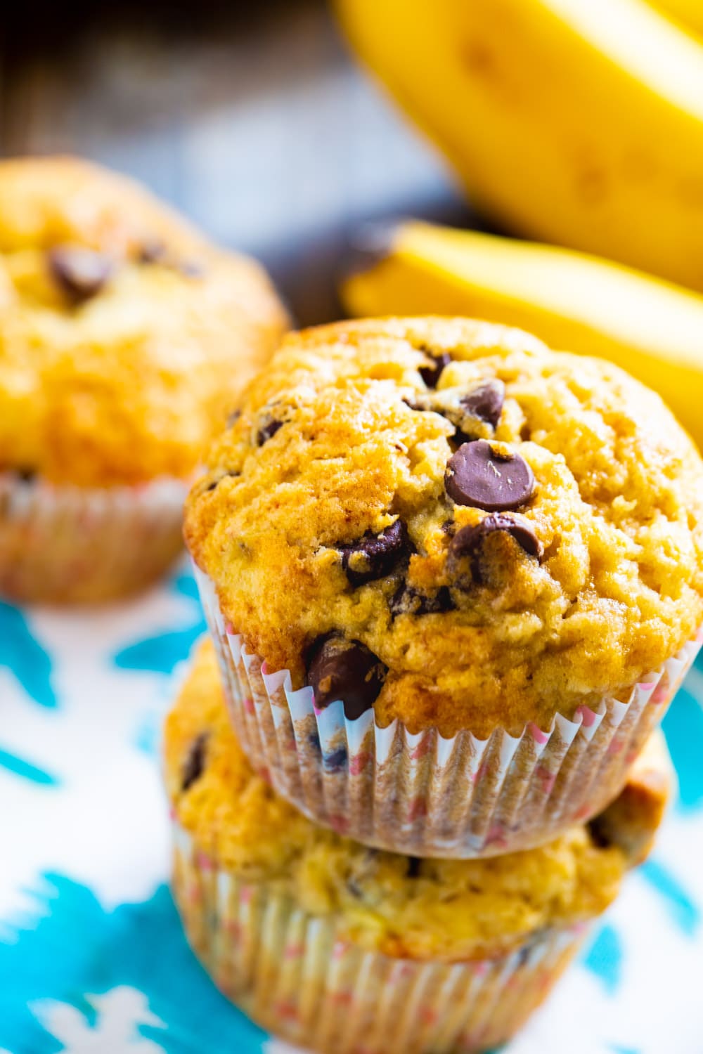 Two muffins stacked on top of each other with fresh bananas in background.