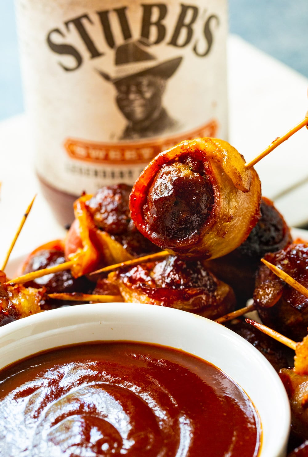 Barbecue Bacon Meatball lifted up to be dipped in barbecue sauce.