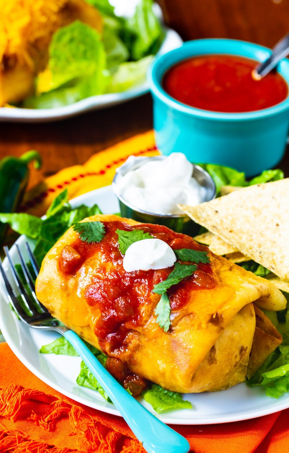 Beef Chimichangas on a plate with bowl of sauce in background.