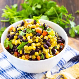 Black Bean and Corn Salsa in a bowl with bunch of cilantro behind it.