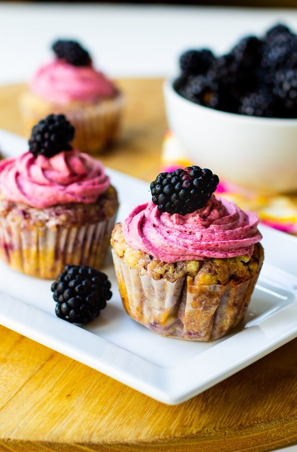 Cupcakes with Blackberries with a bowl of blackberries in background.