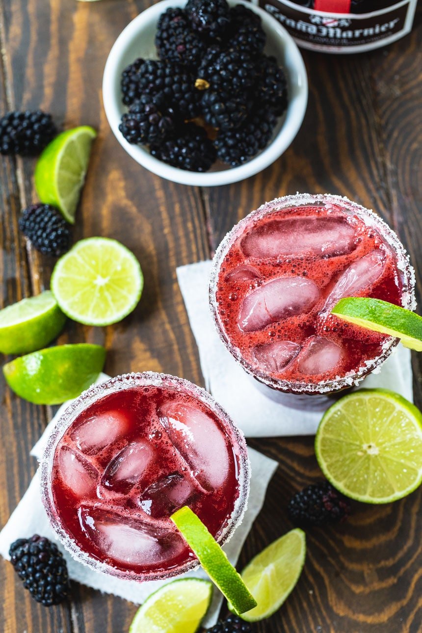 Overhead of Blackberry Margaritas with lime wedges and fresh blackberries scattered around them.