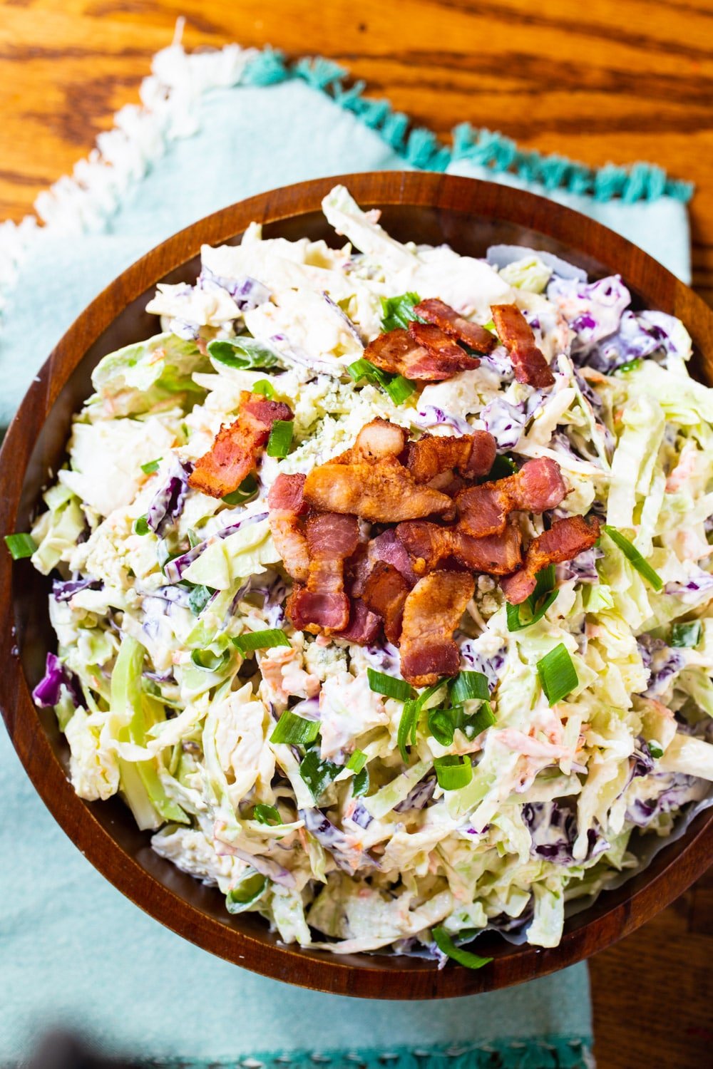 Coleslaw in wooden bowl with bacon crumbles on top.