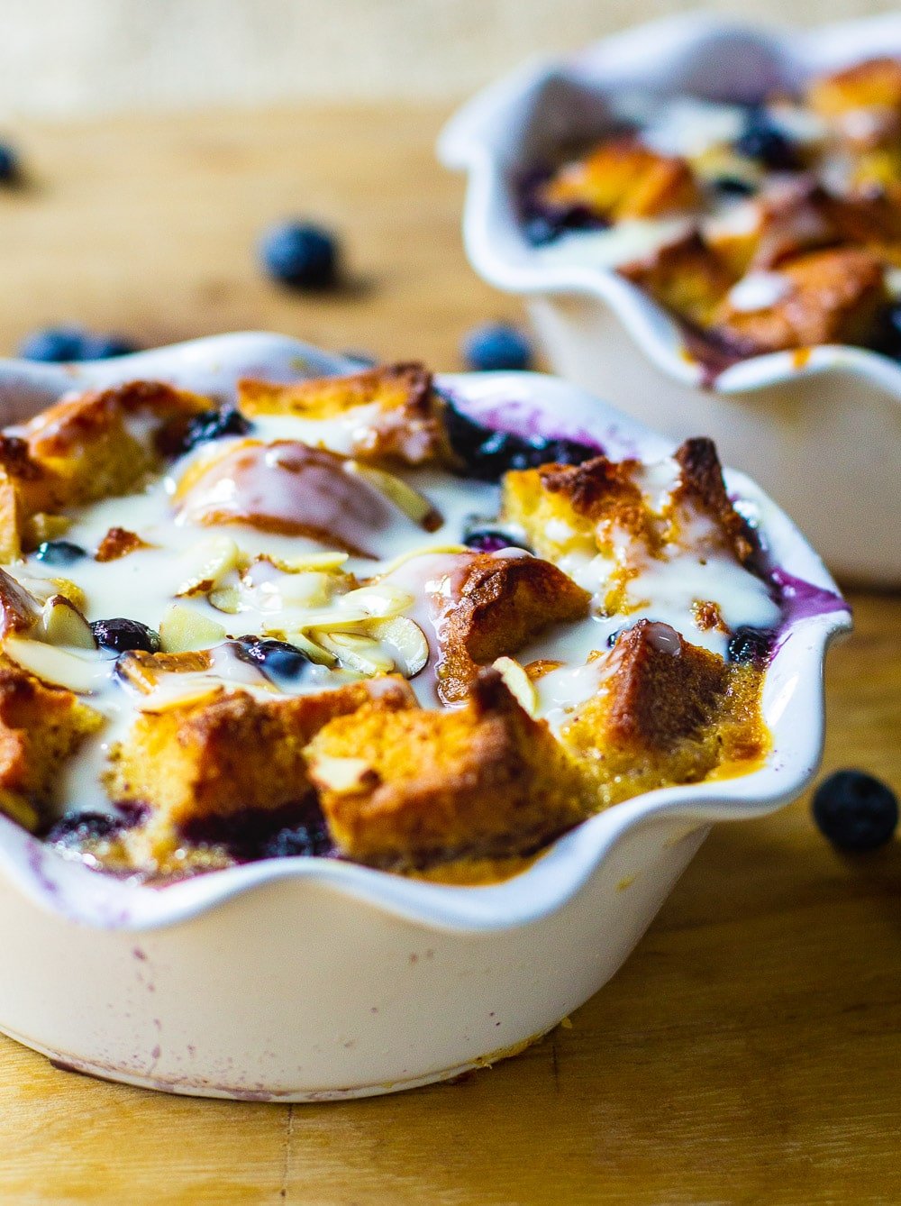 Bread pudding with blueberries in two white ramekins.