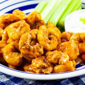 Buffalo Shrimp on a plate with celery and small bowl of dressing.