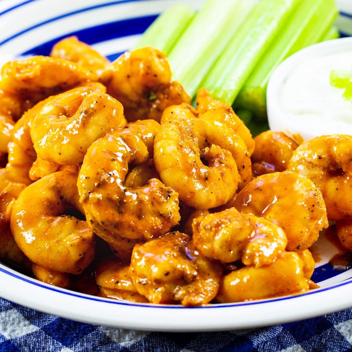 Buffalo Shrimp on a plate with celery and small bowl of dressing.