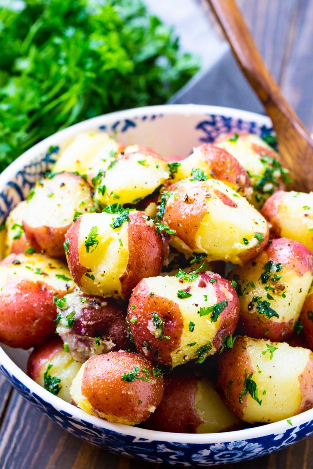 Patatas con mantequilla y perejil en un bol con un manojo de perejil fresco.