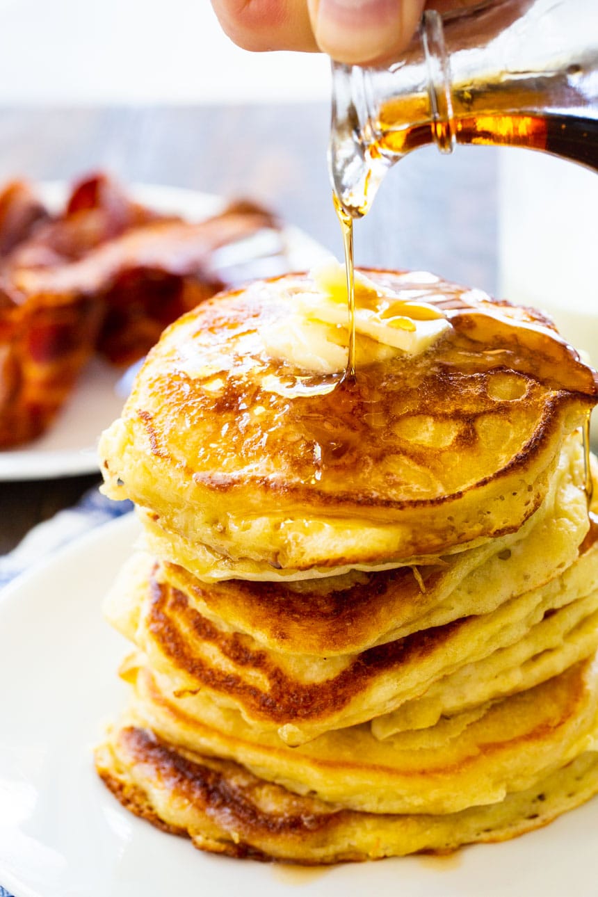 Stack of Buttermilk Pancakes with bacon in the background.