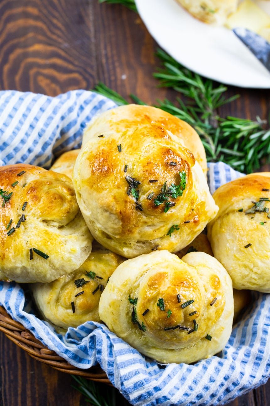Buttery Herb Yeast Rolls in a bread basket with fresh herbs in background.