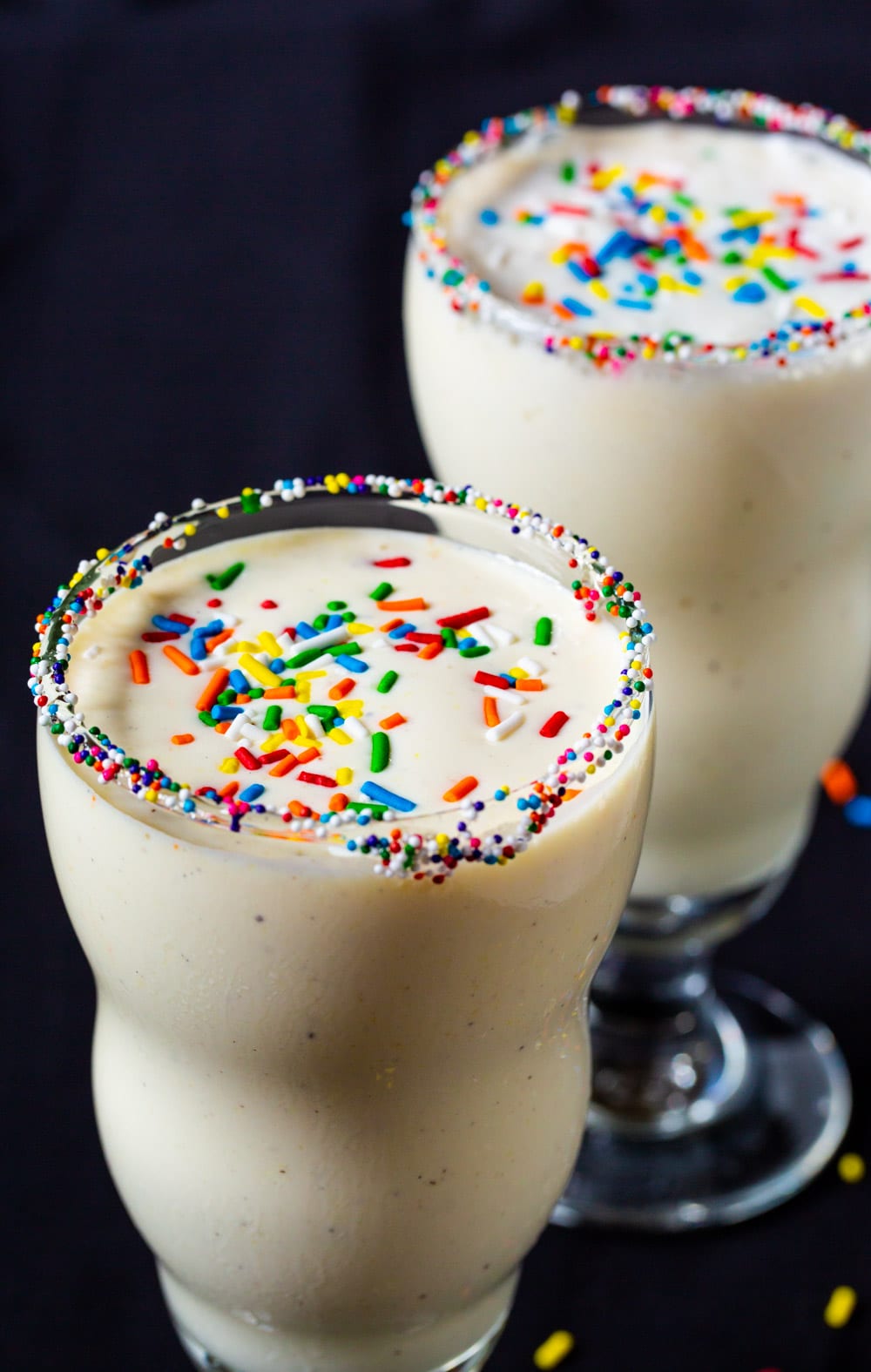 Milkshakes in two glasses with sprinkles on top.