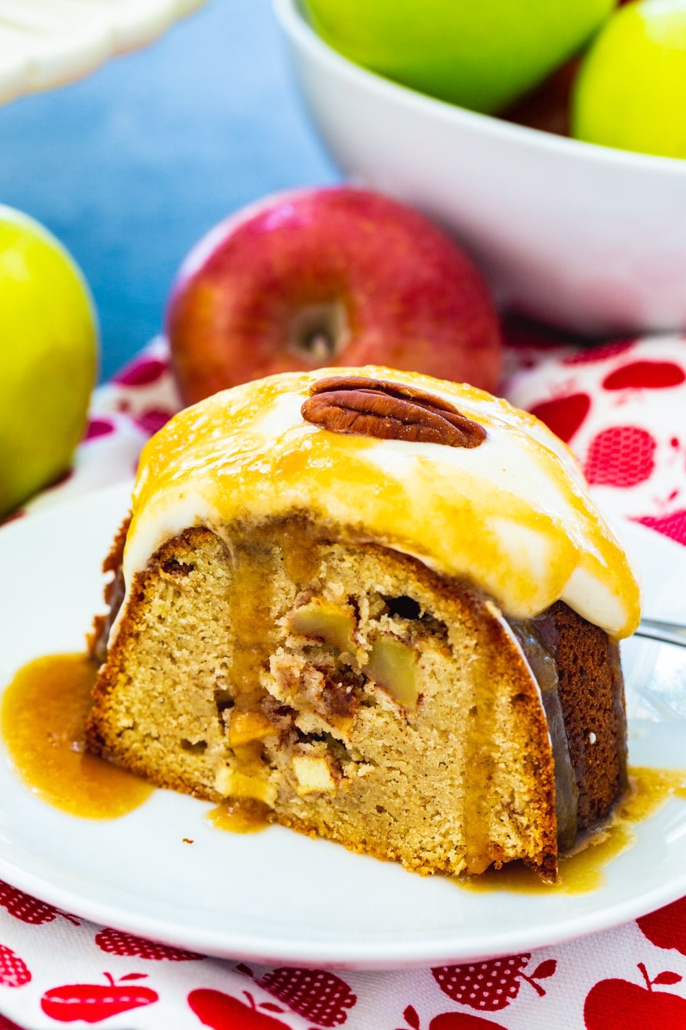 Slice of pound cake on a small plate with fresh apples in background.