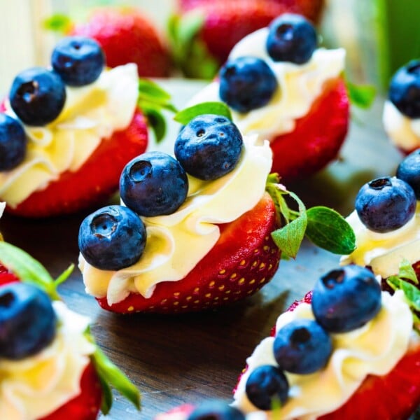 Red, White, and Blue Cheesecake Strawberries on a dark wood board.